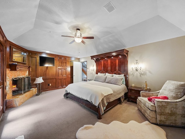 bedroom with lofted ceiling, ceiling fan, a tray ceiling, a fireplace, and light colored carpet