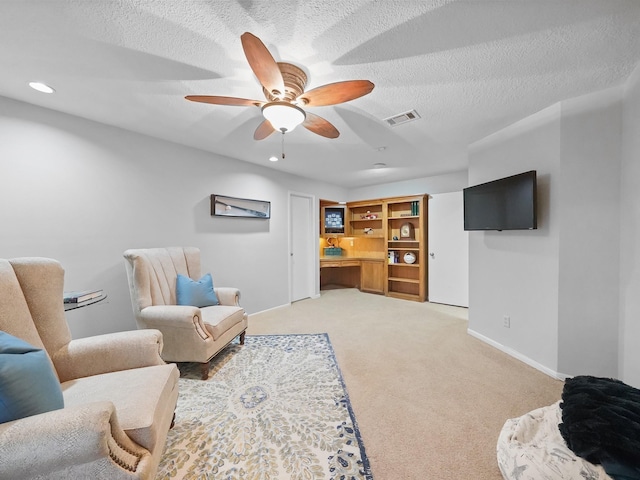 living area featuring ceiling fan, light carpet, and a textured ceiling