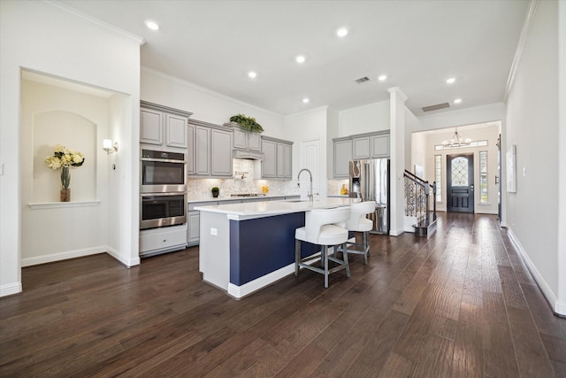 kitchen featuring sink, appliances with stainless steel finishes, a kitchen island with sink, backsplash, and a kitchen breakfast bar