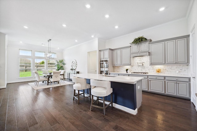 kitchen with a breakfast bar, crown molding, dark hardwood / wood-style floors, gray cabinets, and a kitchen island with sink