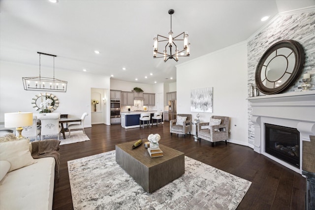 living room with ornamental molding, dark wood-type flooring, a large fireplace, and a chandelier