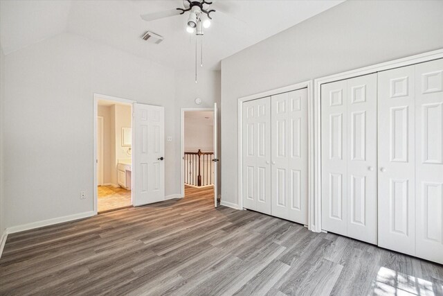 unfurnished bedroom featuring ensuite bath, two closets, a towering ceiling, ceiling fan, and hardwood / wood-style floors