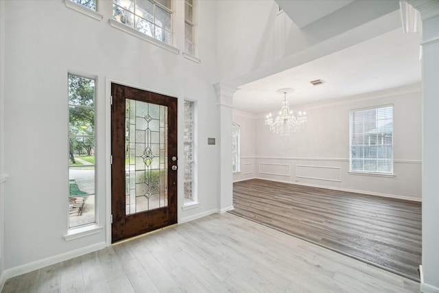 foyer entrance featuring a notable chandelier, light hardwood / wood-style flooring, ornamental molding, and decorative columns