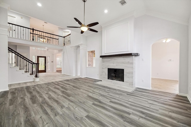 unfurnished living room with a tile fireplace, a towering ceiling, wood-type flooring, ceiling fan, and crown molding