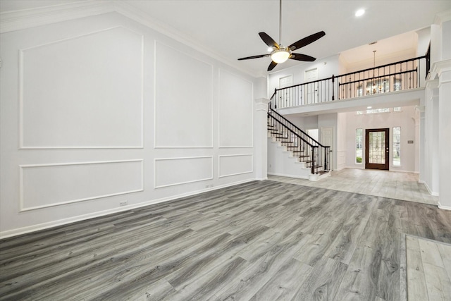 unfurnished living room featuring crown molding, hardwood / wood-style flooring, ceiling fan, and a towering ceiling