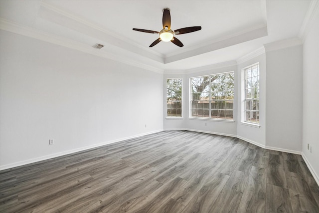 empty room featuring dark wood-type flooring, ceiling fan, a tray ceiling, and crown molding