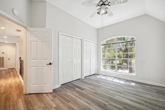 unfurnished bedroom featuring hardwood / wood-style flooring, vaulted ceiling, ceiling fan, and two closets