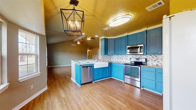 kitchen with lofted ceiling, blue cabinetry, stainless steel appliances, decorative backsplash, and decorative light fixtures