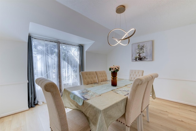 dining area featuring a notable chandelier, vaulted ceiling, and light wood-type flooring