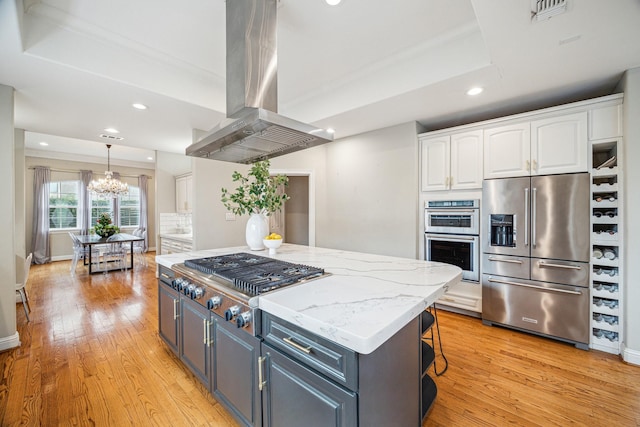 kitchen featuring stainless steel appliances, a center island, island range hood, white cabinets, and decorative light fixtures