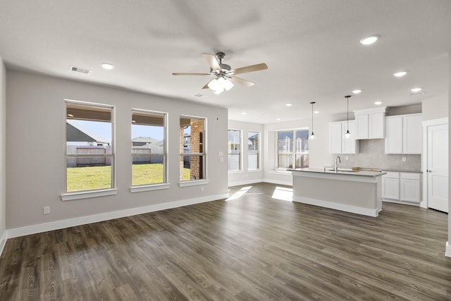 kitchen with white cabinetry, tasteful backsplash, a center island with sink, dark hardwood / wood-style floors, and pendant lighting