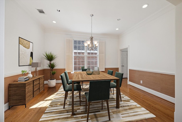 dining room with crown molding, wood-type flooring, and an inviting chandelier