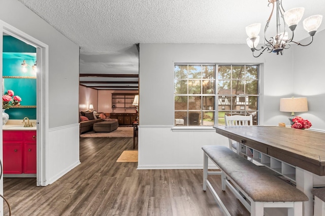 dining space featuring dark hardwood / wood-style floors, sink, a chandelier, beam ceiling, and a textured ceiling