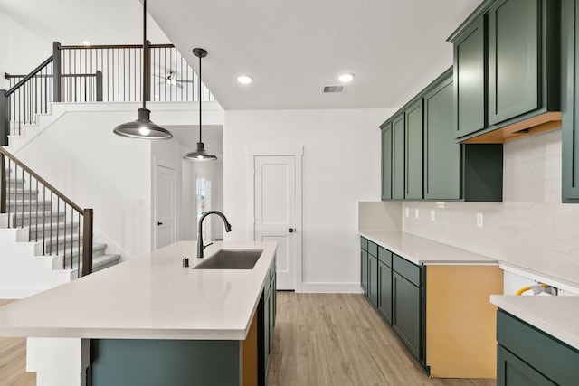 kitchen featuring sink, light hardwood / wood-style flooring, green cabinets, backsplash, and decorative light fixtures