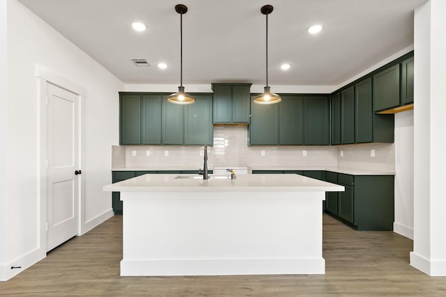 kitchen featuring sink, tasteful backsplash, decorative light fixtures, light hardwood / wood-style flooring, and an island with sink