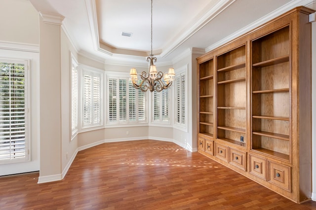 unfurnished dining area with built in features, hardwood / wood-style floors, ornamental molding, a raised ceiling, and a chandelier