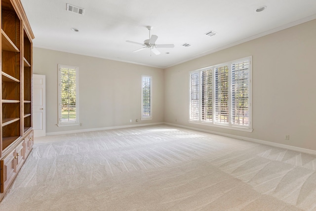 carpeted spare room featuring ceiling fan, crown molding, and a healthy amount of sunlight