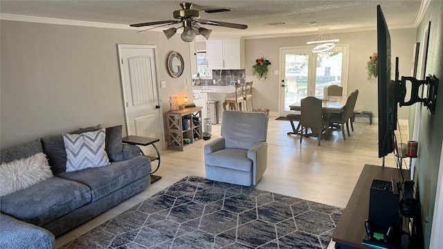 living room featuring ceiling fan, ornamental molding, a textured ceiling, and light wood-type flooring