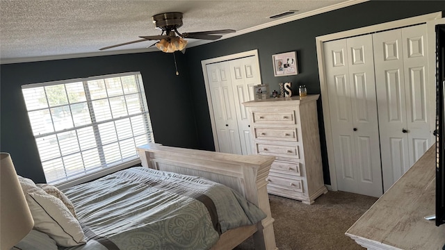 bedroom with multiple closets, carpet floors, a textured ceiling, and ceiling fan