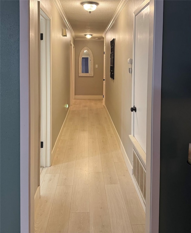 hallway featuring ornamental molding, a textured ceiling, and light wood-type flooring