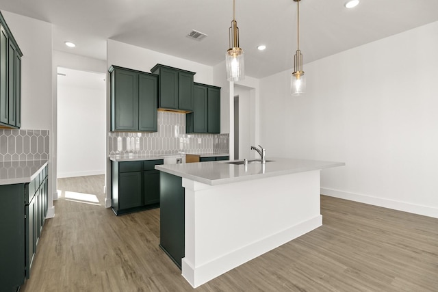 kitchen featuring decorative light fixtures, sink, decorative backsplash, a kitchen island with sink, and light hardwood / wood-style flooring