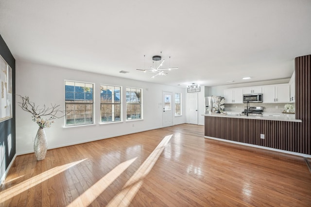 unfurnished living room with an inviting chandelier and light wood-type flooring