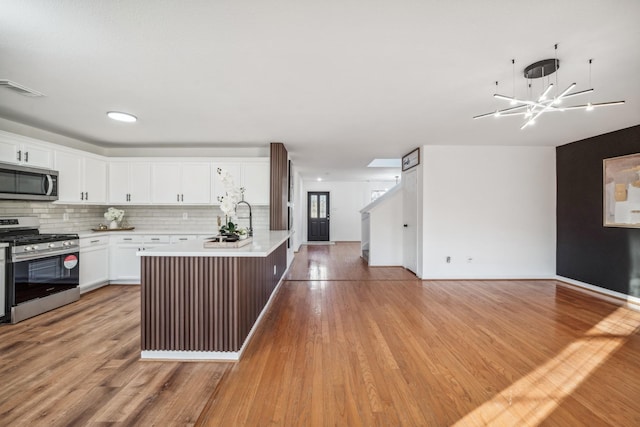 kitchen featuring sink, appliances with stainless steel finishes, a kitchen island with sink, decorative backsplash, and white cabinets