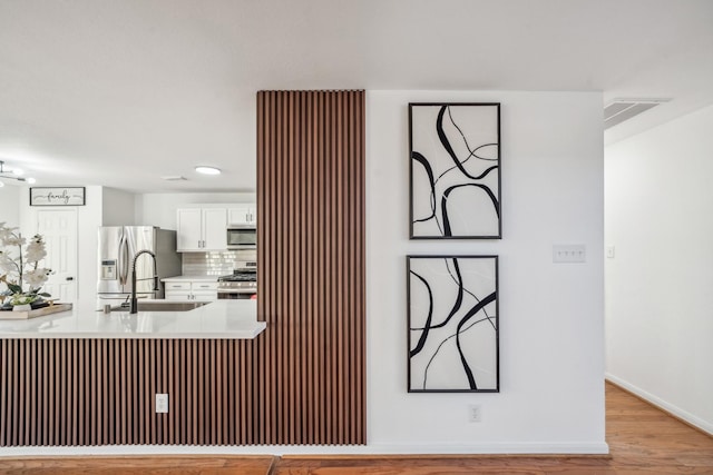 kitchen featuring tasteful backsplash, white cabinetry, sink, stainless steel appliances, and light wood-type flooring