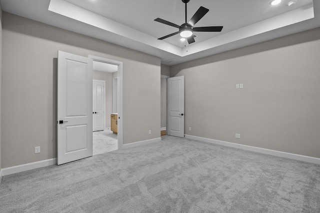 unfurnished bedroom with light carpet, a tray ceiling, and ceiling fan