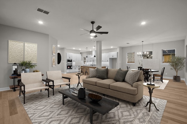 living room with sink, ceiling fan with notable chandelier, and light hardwood / wood-style flooring