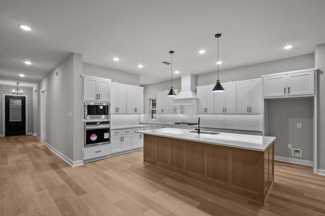 kitchen with premium range hood, appliances with stainless steel finishes, a center island with sink, and white cabinets