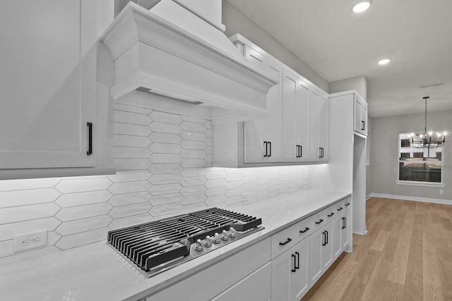 kitchen with premium range hood, stainless steel gas stovetop, white cabinets, backsplash, and hanging light fixtures