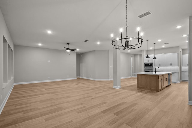 kitchen with sink, white cabinets, hanging light fixtures, a large island, and light hardwood / wood-style flooring