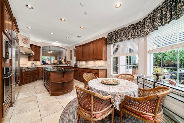 kitchen with tasteful backsplash, ornamental molding, stainless steel appliances, and wall chimney exhaust hood