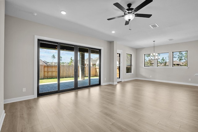 unfurnished living room featuring ceiling fan with notable chandelier, plenty of natural light, and light hardwood / wood-style floors