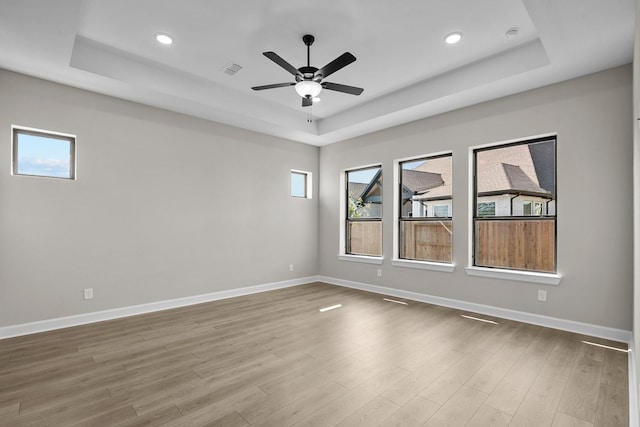 empty room with hardwood / wood-style floors, ceiling fan, and a tray ceiling