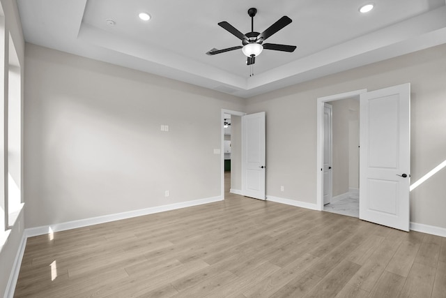 unfurnished bedroom featuring a tray ceiling, light hardwood / wood-style floors, and ceiling fan