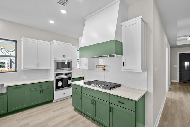 kitchen with premium range hood, green cabinets, stainless steel appliances, decorative backsplash, and white cabinets