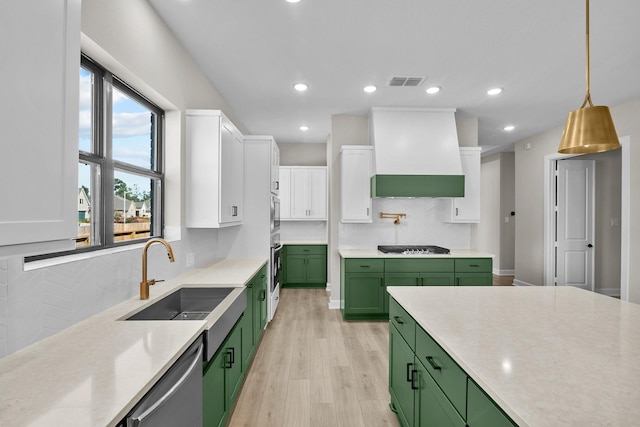 kitchen featuring sink, white cabinetry, green cabinets, custom range hood, and stainless steel appliances