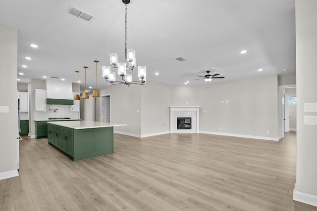 kitchen with pendant lighting, a fireplace, custom range hood, green cabinetry, and a kitchen island