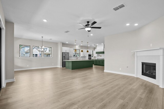 unfurnished living room with ceiling fan with notable chandelier and light hardwood / wood-style flooring