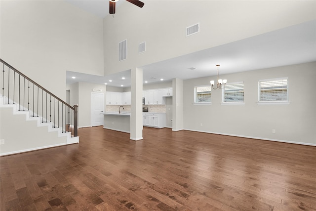 unfurnished living room with a high ceiling, sink, ceiling fan with notable chandelier, and dark hardwood / wood-style flooring