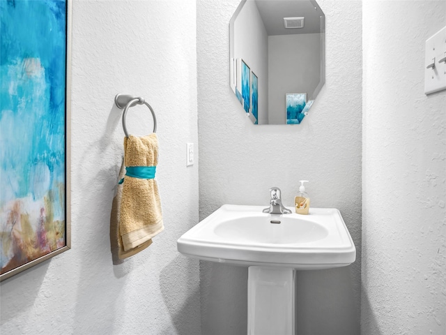 bathroom featuring a textured wall, a sink, and visible vents