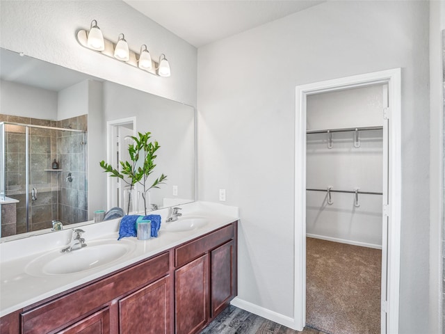 bathroom featuring double vanity, a shower stall, a walk in closet, and a sink