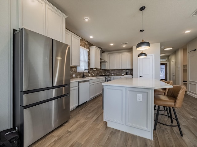 kitchen featuring decorative light fixtures, a kitchen island, white cabinets, stainless steel appliances, and backsplash