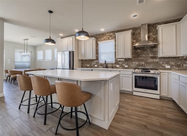 kitchen featuring a kitchen island, pendant lighting, white cabinets, stainless steel appliances, and wall chimney range hood