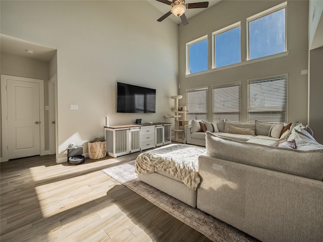 living room featuring ceiling fan, a high ceiling, and light wood-type flooring