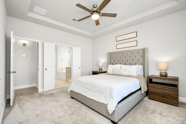 carpeted bedroom with a raised ceiling, ceiling fan, and ensuite bath