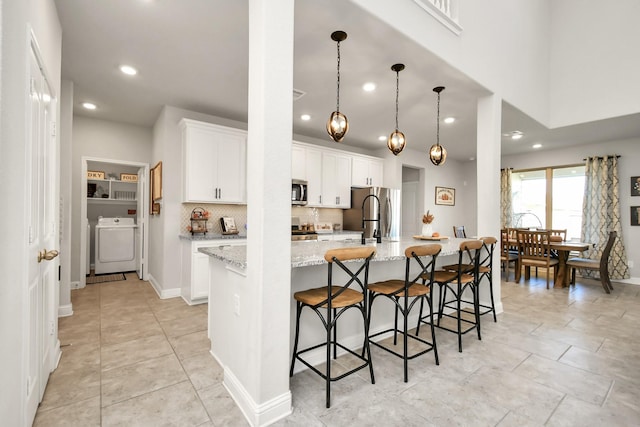 kitchen with appliances with stainless steel finishes, washer / dryer, white cabinets, and a spacious island