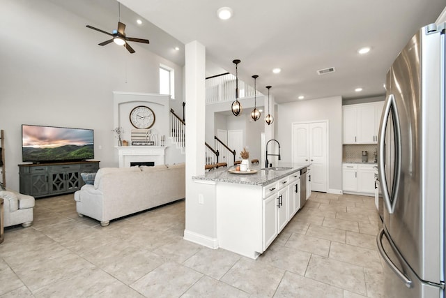 kitchen with sink, stainless steel refrigerator, pendant lighting, light stone countertops, and white cabinets